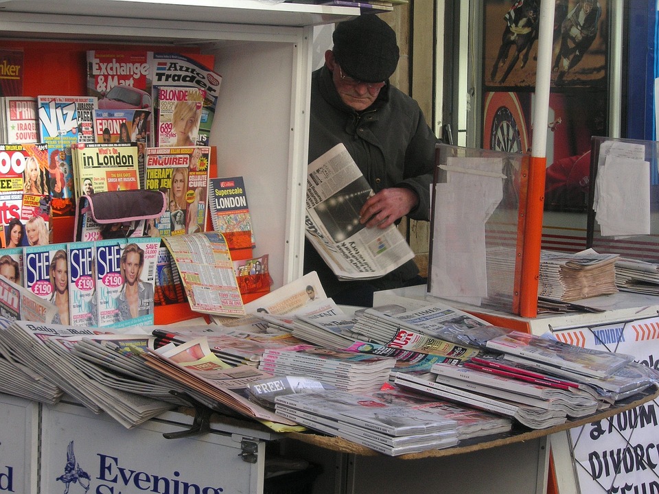 edicola con varie riviste esposte e un cliente con in mano un quotidiano