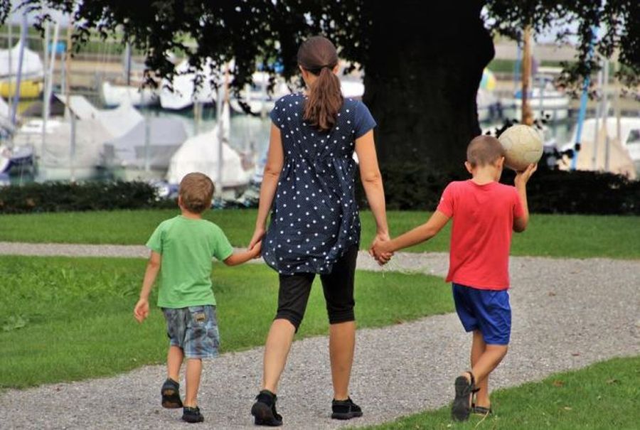 una madre che passeggia al parco tenendo per mano i due figli