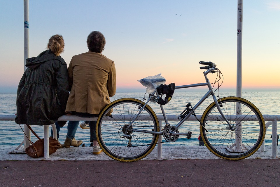 una coppia seduta in riva al mare con la bicicletta poggiata alla panchina