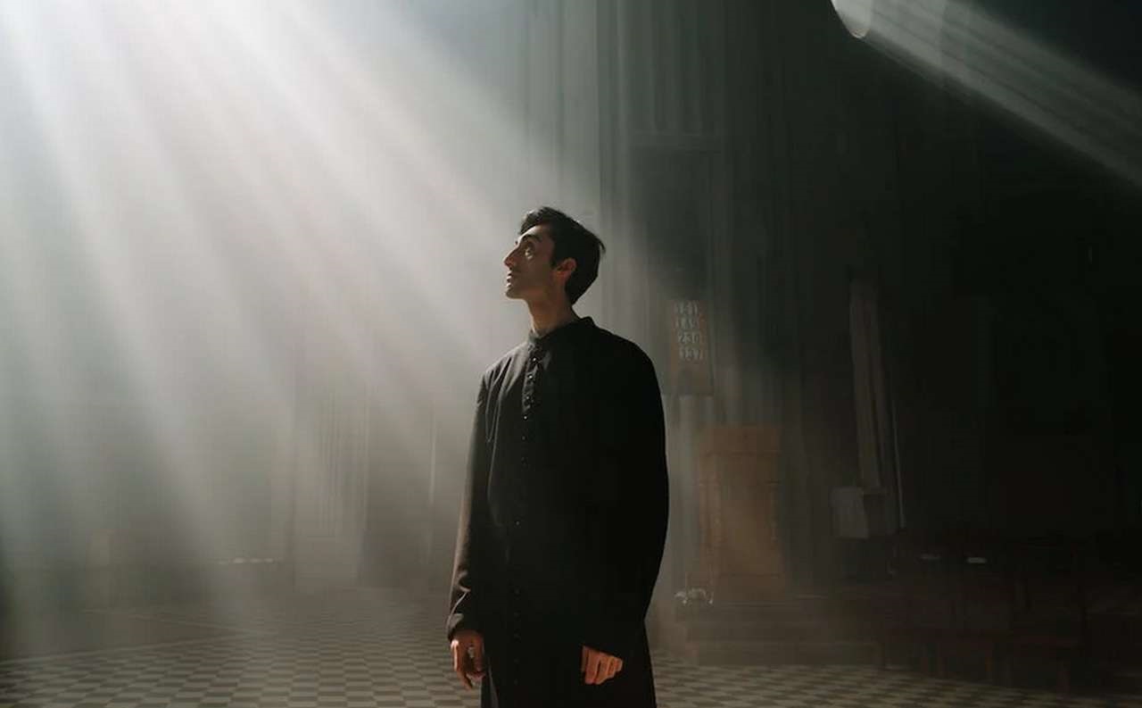 un prete investito da un fascio di luce che penetra in una chiesa attraverso i rosoni