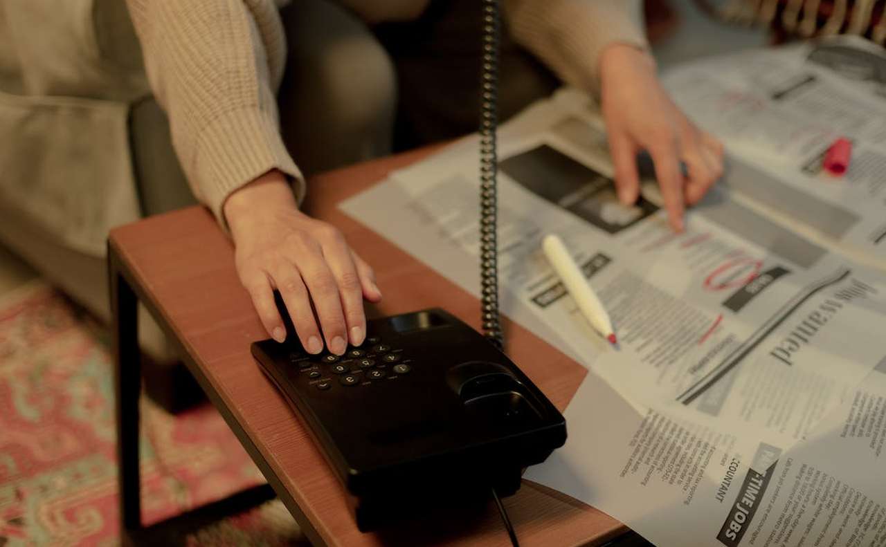 una donna che compone dei numeri al telefono mentre cerchia alcuni annunci sul giornale