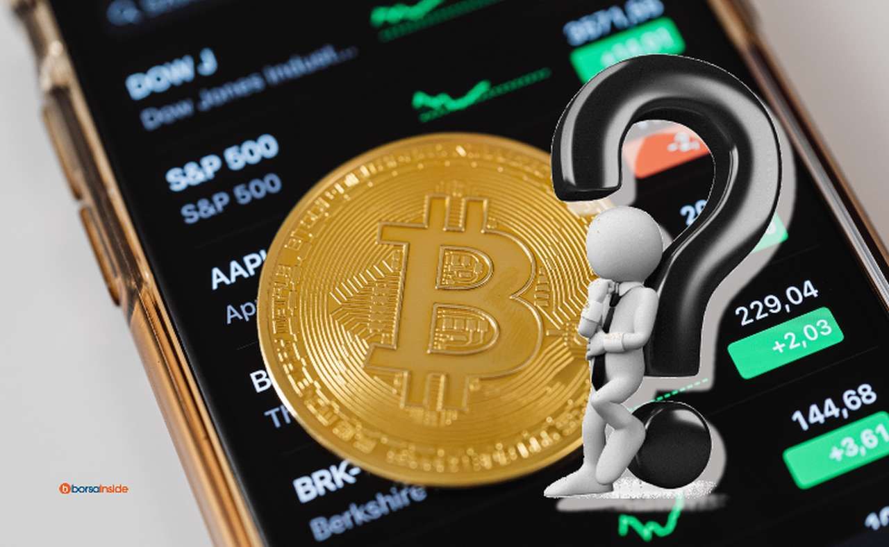 lo schermo di uno smartphone con grafici sull'andamento delle crypto, una moneta di Bitcoin e un punto interrogativo in sovrimpressione